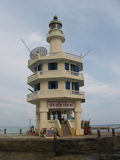 a tall white building sitting on top of a pier next to the ocean with people standing around it