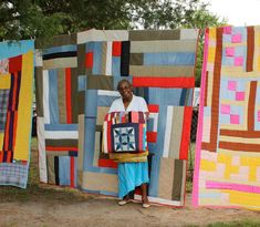 a woman standing in front of quilts hanging on the side of a tree line