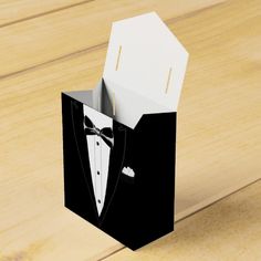 an open black and white paper box with a bow tie on the inside, sitting on a wooden surface