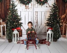 a little boy sitting on a chair in front of some christmas trees and lanterns with lights