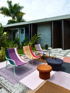 colorful lawn chairs and tables in front of a house with palm trees on the side