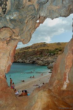 people are on the beach and in the water near some large rocks, while one person is swimming