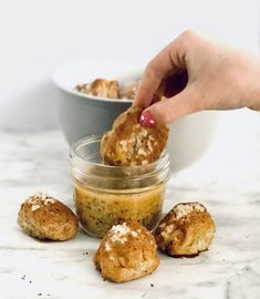 a person dipping some food into a small glass jar on top of a marble counter