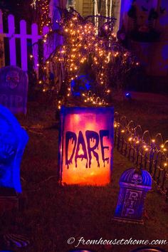 a yard decorated for halloween with lights and tombstones in the foreground, and a sign that says dare on it