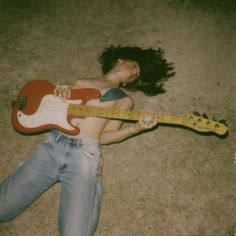 a woman laying on the floor with her guitar and head resting on her stomach,