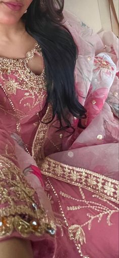 a woman in a pink and gold dress sitting on a bed with her hair down