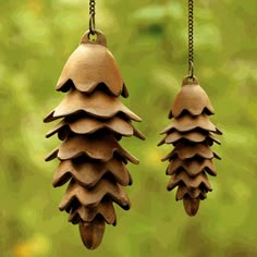 two wooden pine cones hanging from chains in front of a green background with trees and grass