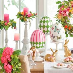 an assortment of decorative easter eggs on a table with flowers and candles in the background