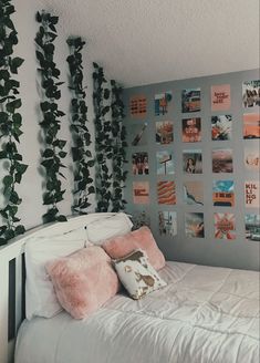 a white bed topped with lots of pillows next to a wall covered in pictures and plants