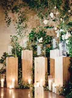 candles are lined up on wooden blocks with greenery and flowers behind them in front of a wall