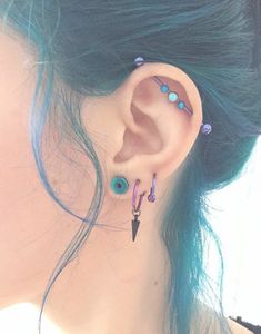 a woman with blue hair has two piercings on her ear and is wearing a pair of earrings