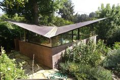 a house in the middle of some trees and bushes with a roof over it's entrance