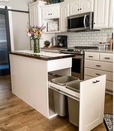 an open cabinet in the middle of a kitchen with two trash cans and a flower vase