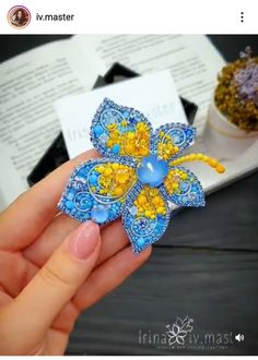 a hand holding a blue and yellow flower brooch