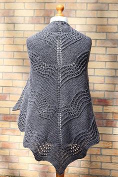 a gray knitted shawl on top of a mannequin dummy with a brick wall in the background