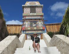 a woman sitting on the steps to a building with a beer in front of her