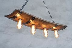 a wooden light fixture with five lights hanging from it's sides and an iron chain