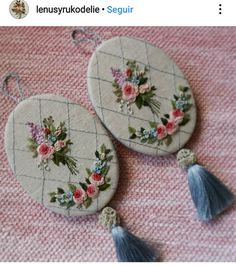 two handmade earrings with flowers and tassels on them are sitting on a pink blanket