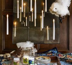 candles are lit on the wall above a table with plates and bowls in front of it