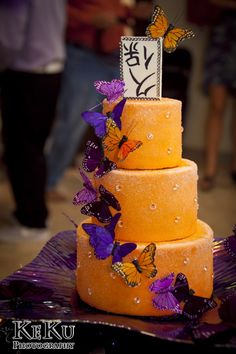 a three tiered cake with purple butterflies on it and a sign that says love