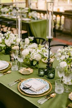 the table is set with green linens and gold place settings, white flowers on each plate