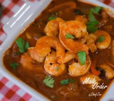 a white bowl filled with shrimp and red pepper sauce on top of a checkered table cloth