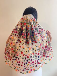 a woman wearing a white dress with colorful flowers on it's cape over her head