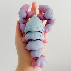 a hand holding a small plastic toy in the shape of a sea creature with pink and blue colors