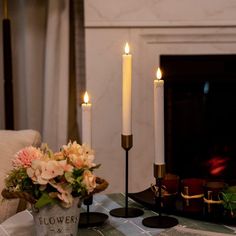 two candles are sitting on a table with flowers and other decorations in front of a fireplace