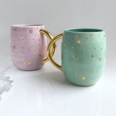 two coffee mugs sitting next to each other on a white counter top with gold stars painted on them