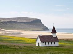 a small white church with a steeple in the middle of an open field next to a body of water