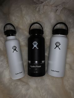 three hydro flasks sitting on top of a white fur covered floor