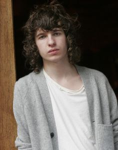 a young man with curly hair standing in front of a door