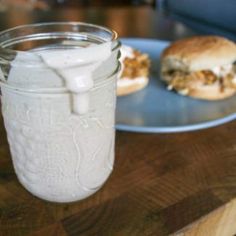 a glass jar filled with milk sitting on top of a table next to a sandwich