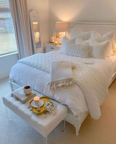 a white bed sitting in a bedroom next to a window with lots of pillows on top of it