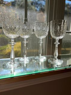 four crystal goblets are lined up on a glass shelf in front of a window