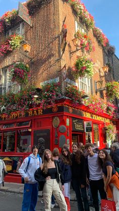 a group of people standing in front of a building with flowers growing on the side