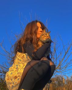 a woman sitting on the ground holding a cat in her lap and looking up into the sky