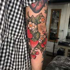 a woman's arm with flowers and strawberries on it, next to a black and white checkered wall