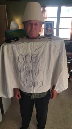 an older man wearing a white hat and holding up a t - shirt that says one night stand