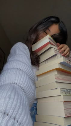 a woman is hiding behind a stack of books with her head on top of each other