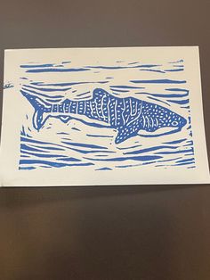 a blue and white drawing of a fish swimming in the water on a brown surface