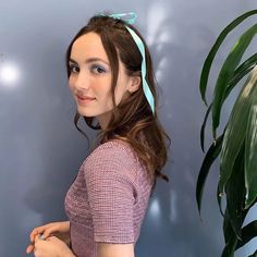 a woman standing next to a green plant wearing a blue ribbon around her head and looking at the camera