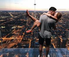 a man and woman kissing on top of a skyscraper