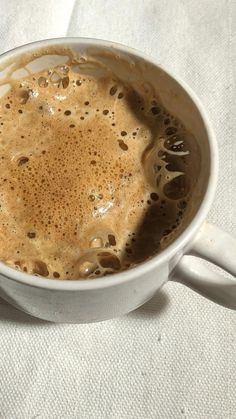 a white cup filled with liquid on top of a cloth covered table next to a spoon