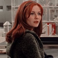 a woman with long red hair standing in front of a counter