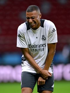 a man standing on top of a soccer field holding his hands in his pockets and smiling