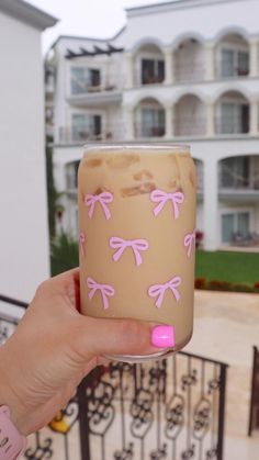 a person holding up a cup with pink bows on it and some buildings in the background