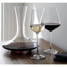 three wine glasses sitting on top of a wooden table next to a decanter