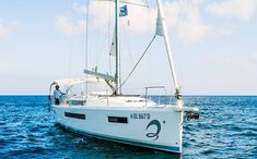 a white sailboat floating on top of the ocean next to a man standing on it